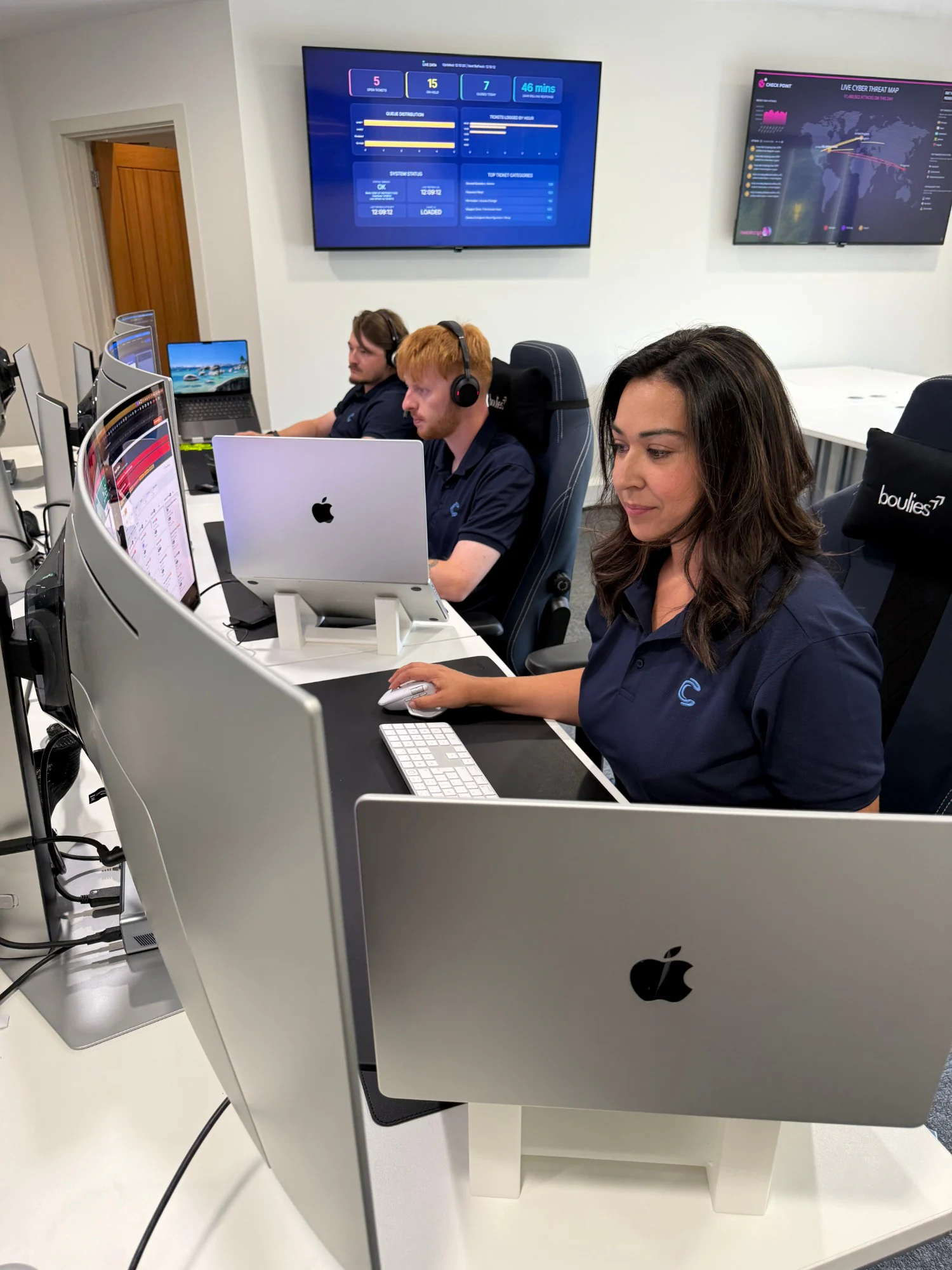 We C2 IT engineers on headsets at the service desk, with live service dashboards on the wall