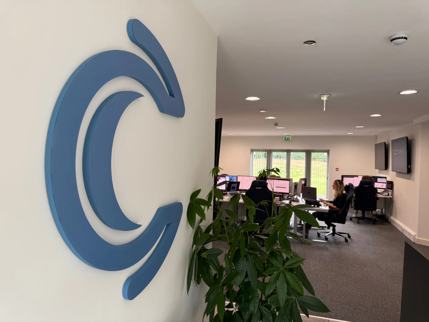 The C2 mark on the office wall with the We C2 IT team at work behind